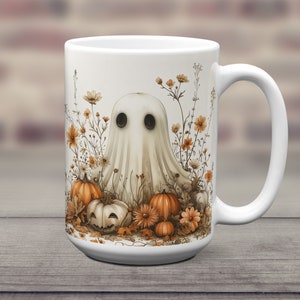 K&ouml;nnte beinhalten: Eine wei&szlig;e Keramiktasse mit einer Geisterillustration, umgeben von K&uuml;rbissen und Blumen. Der Geist ist wei&szlig; mit schwarzen Augen und einem schwachen L&auml;cheln. Die K&uuml;rbisse sind orange und braun, einige sind zu Jack-o'-Lanterns geschnitzt. Die Blumen sind gelb und orange.