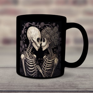 May include: Black coffee mug with a white and gray illustration of two skeletons embracing. The skeletons are surrounded by roses and vines.