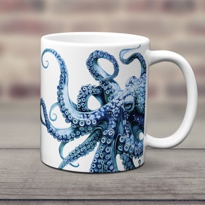 May include: A white ceramic mug featuring a detailed illustration of a blue octopus with prominent suckers on its tentacles. The octopus design wraps around the side of the mug, showcasing intricate shading and a realistic marine creature aesthetic.
