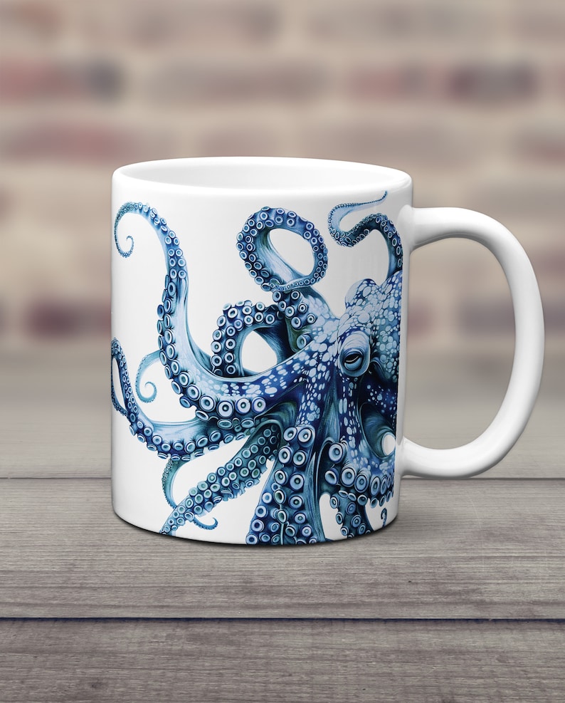 May include: A white ceramic mug featuring a detailed illustration of a blue octopus with prominent suckers on its tentacles. The octopus design wraps around the side of the mug, showcasing intricate shading and a realistic marine creature aesthetic.