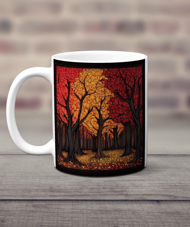 K&ouml;nnte beinhalten: Wei&szlig;e Keramiktasse mit einem bunten Herbstwaldmotiv. Die B&auml;ume sind eine Mischung aus roten, orangefarbenen und gelben Bl&auml;ttern. Der Waldboden ist mit heruntergefallenen Bl&auml;ttern bedeckt.