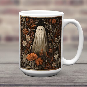 May include: White ceramic mug with a vintage illustration of a ghost in a floral garden. The design features orange, brown, and white flowers against a black background. The mug has a large handle and a glossy finish.