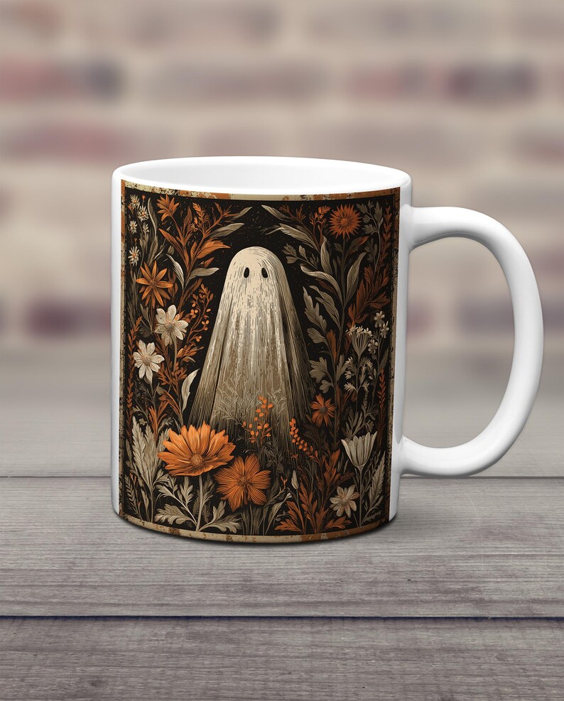 May include: White ceramic mug with a vintage illustration of a ghost amidst orange, brown, and white flowers on a black backdrop. The mug has a white handle. The mug is set on a wooden surface.