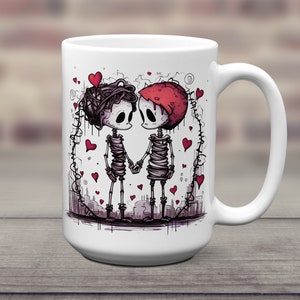 May include: White ceramic coffee mug with a graphic of two skeletons holding hands. The skeletons are wrapped in bandages and have hearts around them. The mug has a black handle.