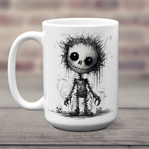 May include: White ceramic coffee mug with a black and white illustration of a cartoon skeleton with a stitched-up body and a toothy grin. The skeleton is standing on a white background with two small skulls on either side.