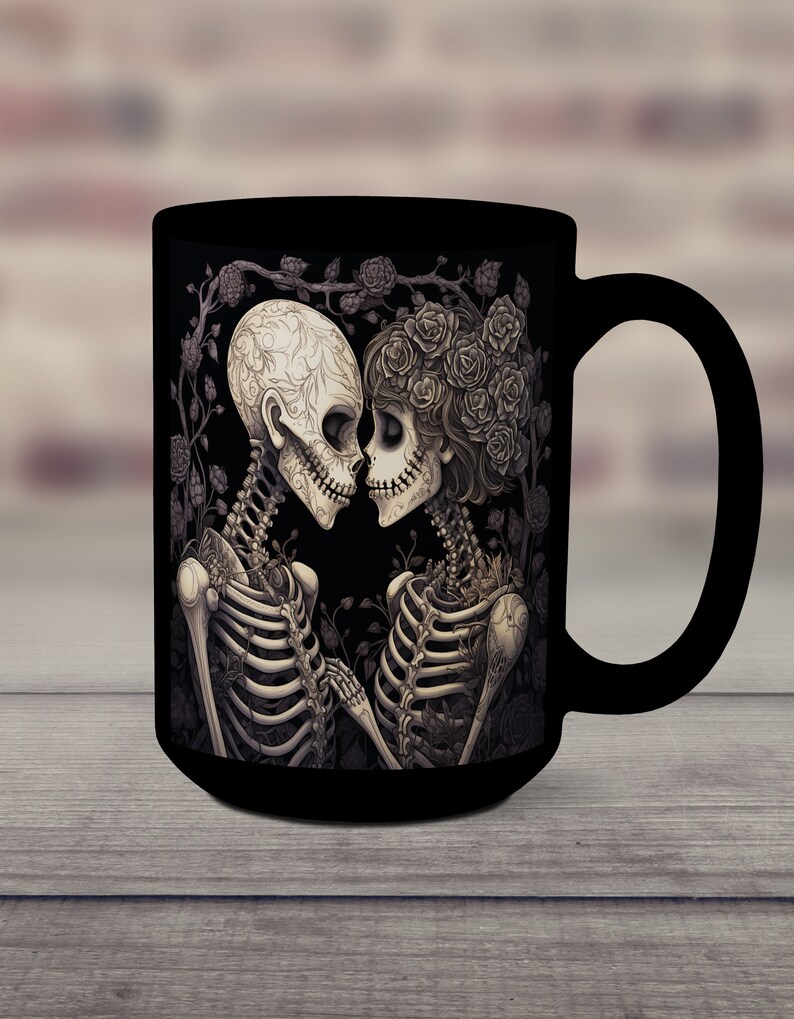 May include: Black coffee mug with a graphic of two skeletons embracing, surrounded by roses and vines. The skeletons are wearing floral crowns and are looking at each other.
