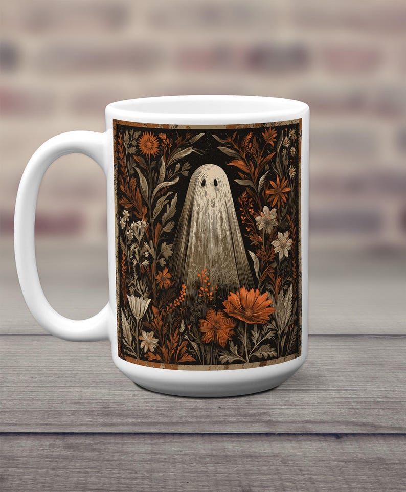 May include: White ceramic mug with a vintage illustration of a ghost in a floral garden. The design features orange and white flowers on a black background. The mug has a large handle and is set against a wooden surface.
