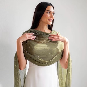 May include: An olive green shawl with a delicate, shimmering pattern of small, scattered silver dots. The sheer fabric drapes elegantly, creating a flowing silhouette. The shawl is worn over a white dress.