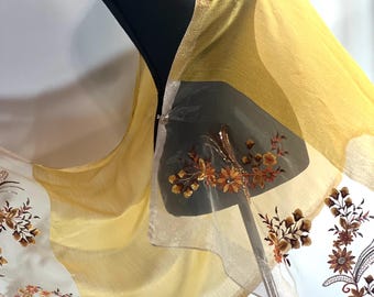 May include: A sheer yellow scarf with gold embroidery of floral designs. The scarf is draped over a black mannequin.