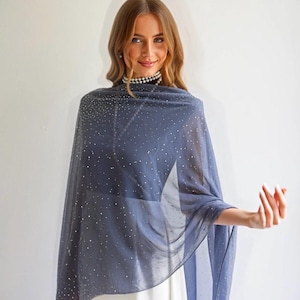 May include: A sheer, navy blue shawl with scattered silver glitter. The shawl is draped over the shoulders, creating a flowing effect. The fabric appears lightweight and delicate, suitable for formal occasions or adding a touch of elegance to an outfit.