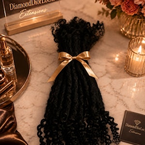 May include: A bundle of black curly hair extensions tied with a gold ribbon. The extensions are displayed on a marble surface, alongside a sign that reads "DiamondDiorLocxs Extensions". A small card with the same logo is also visible.