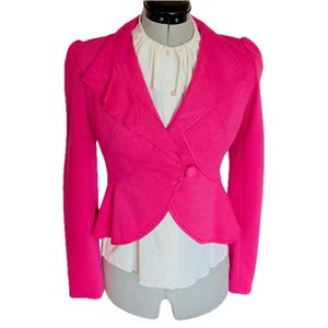 May include: A bright pink blazer with a peplum hem and a single button closure. The jacket has long sleeves and a tailored fit. A white blouse is visible underneath the blazer.