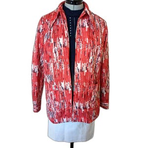 Puede incluir: Chaqueta vintage estampada en rojo, blanco y azul marino, con cuello y dos bolsillos delanteros. La chaqueta abierta revela un suéter azul oscuro. La prenda se exhibe en un maniquí.