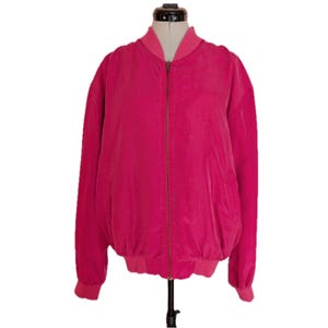 May include: A bright pink bomber jacket with a zip-up front, ribbed cuffs, and a ribbed collar. The jacket is displayed on a mannequin and has a soft, velvety texture. The jacket has two front pockets.