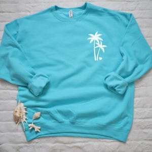 May include: A turquoise blue sweatshirt with a white palm tree design and a small heart on the left chest.