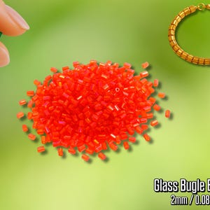 Puede incluir: Un conjunto de cuentas de vidrio tubular rojo vibrante, 2 mm (0,2 cm), con una pulsera dorada. Una mano sostiene una sola cuenta verde. El fondo es un degradado de verde.
