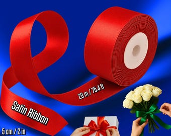May include: A roll of red satin ribbon with the text "Satin Ribbon" and measurements of 5 cm / 2 in. The ribbon is 23 m / 75.4 ft long. The image also shows a bouquet of white roses and a gift box with a red bow.