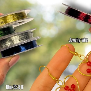 Può includere: Bobine di filo per gioielli in vari colori, tra cui oro, verde, argento e blu. L'immagine mostra anche orecchini a forma di cuore con perline rosse. Il testo "Jewelry wire" e "10m/32.8 ft" sono visibili.