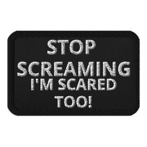 May include: Black rectangular patch with white embroidered text that reads "STOP SCREAMING I'M SCARED TOO!". The patch has a black border and is likely designed to be sewn or ironed onto fabric.