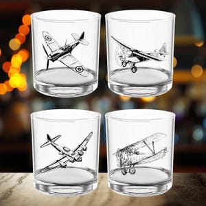 May include: Set of four clear glass tumblers with black and white illustrations of vintage airplanes. Each tumbler features a different airplane design.