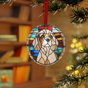 Könnte beinhalten: Runder Weihnachtsschmuck mit einem Cavalier King Charles Spaniel Hund im Buntglas-Design. Der Anhänger hat ein rotes Band zum Aufhängen und ist vor einem verschwommenen Hintergrund aus Weihnachtsbaum und Bücherregal platziert.