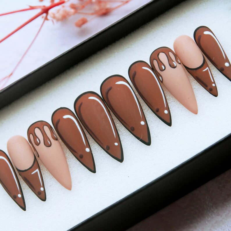 May include: Set of ten false nails in a brown and nude colour scheme. The nails are long and have a pointed shape. Some of the nails feature a brown drip design.