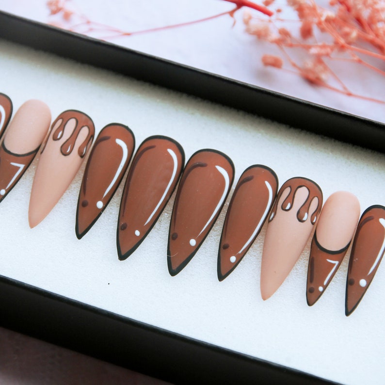 May include: Set of ten false nails with a brown and white drip design. The nails are long and almond shaped.