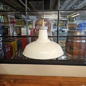 May include: White enamel pendant light with a black cord and a brass socket. The light is hanging from a black metal ceiling fixture.