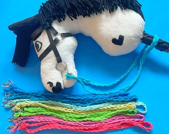 May include: A white and black stuffed horse head with a black bridle and a heart on the side. The horse is attached to a blue braided rope with a metal clip. There are 10 additional braided ropes in various colors, including blue, green, yellow, and pink, all with metal clips.