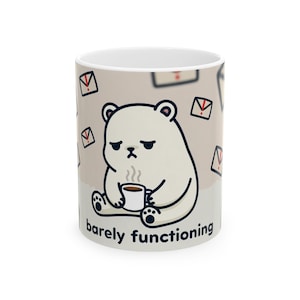 May include: White ceramic mug with a cartoon polar bear, looking unhappy, holding a coffee cup. The mug has the words "barely functioning" and is decorated with envelope icons.