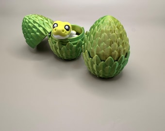 May include: Three-dimensional green egg-shaped containers with a textured surface. One egg is open, revealing a yellow and white snake figurine inside. The other two eggs are closed or partially open. The background is a solid light gray.