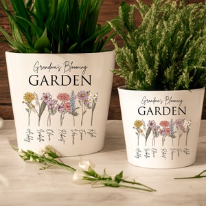 May include: Two white ceramic flower pots with the text "Grandma's Blooming Garden" and a floral design. The smaller pot has the names "Lily, Emma, Robert, Olivia, Jacob, Abby" written on it. The larger pot has the names "Lily, Emma, Robert, Olivia, Jacob, Abby" written on it.