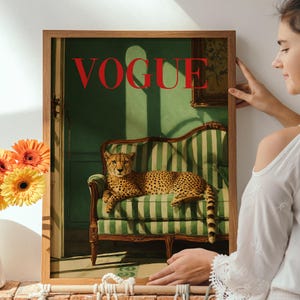 May include: A framed wall art print featuring a cheetah resting on a green and white striped sofa. The word VOGUE is printed in large red capital letters at the top. The scene is set in a room with green walls and a wooden door frame visible.