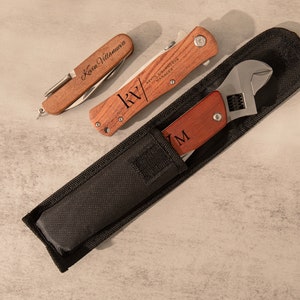 May include: A set of three tools in a black nylon pouch. The tools include a wrench, a pocket knife with a wooden handle engraved with "KV" and "SANTA BARBARA MANAGER", and a smaller pocket knife with a wooden handle engraved with "Kevin Villanueva".