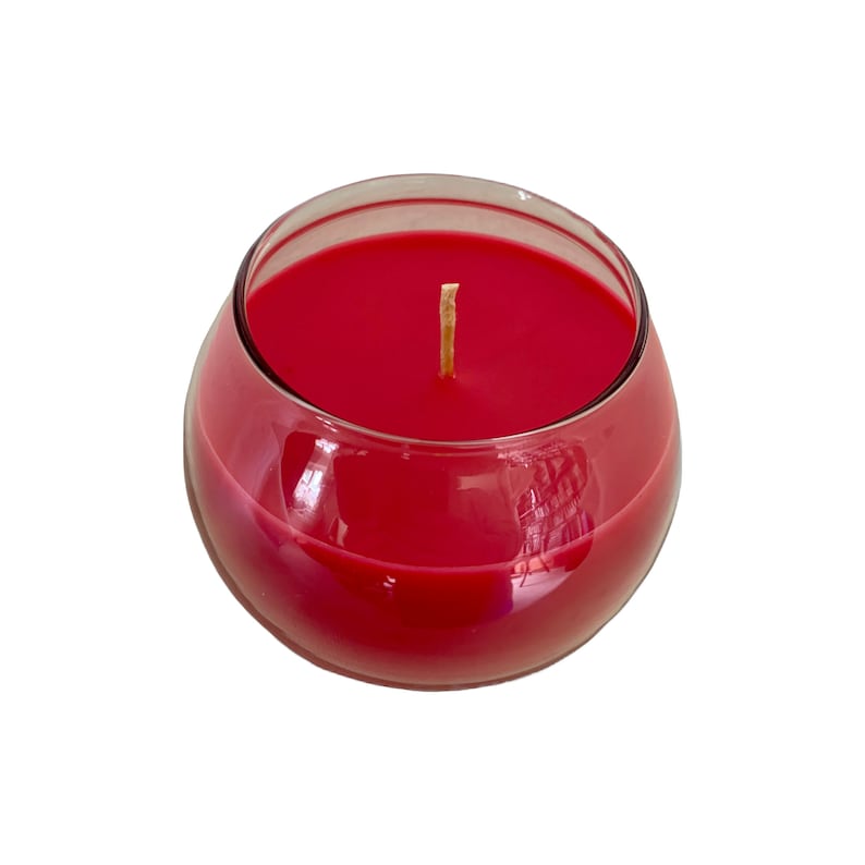 May include: A round, red candle in a clear glass container. The candle has a smooth surface and a single, light-colored wick. The glass has a curved shape, and the candle appears to be unscented.