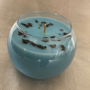 Pode incluir: Um casti&ccedil;al redondo de vidro transparente preenchido com cera azul clara. A vela tem um pavio de madeira e &eacute; decorada com pequenos peda&ccedil;os castanhos escuros. A vela &eacute; um item decorativo.