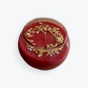 Op de afbeelding: Een rode kaars met gouden vlokken in een glazen pot.