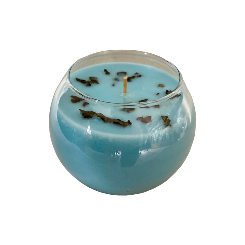 Pode incluir: Um casti&ccedil;al redondo de vidro transparente preenchido com cera azul clara. A vela tem um pavio de madeira e &eacute; decorada com pequenas folhas secas castanhas escuras. Um elemento decorativo para a casa.
