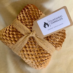 May include: A square package wrapped in brown honeycomb paper and tied with twine. A tag with the text "CLACHAIG CANDLES scottish island scents" is attached. The package is on a beige surface.