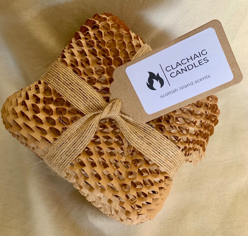 May include: A square package wrapped in brown honeycomb paper and tied with twine. A tag with the text "CLACHAIG CANDLES scottish island scents" is attached. The package is on a beige surface.