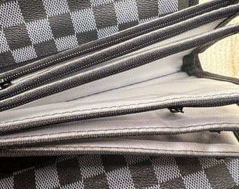 May include: A black and white checkered wallet with multiple zippered compartments. The wallet is open to reveal a gray fabric lining.