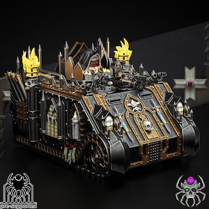 Op de afbeelding: Een zwart en gouden miniatuur oorlogvoertuig met gotische details, waaronder een gekapte figuur en een toren met vlammen. Het voertuig heeft een schedel en gekruiste beenderen symbool aan de voorkant.