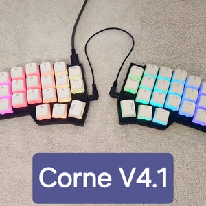 May include: A split keyboard with a white and black design. The keyboard has a variety of colored keys, including pink, blue, green, and yellow. The keyboard is labeled "Corne V4.1".