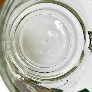 May include: A clear glass mug base featuring a circular design with the number 15, a small square logo, and the text USA embossed in the center. The glass is transparent with a smooth, rounded bottom surface and a visible handle attachment point.