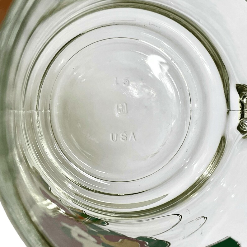 May include: A clear glass mug base featuring a circular design with the number 15, a small square logo, and the text USA embossed in the center. The glass is transparent with a smooth, rounded bottom surface and a visible handle attachment point.