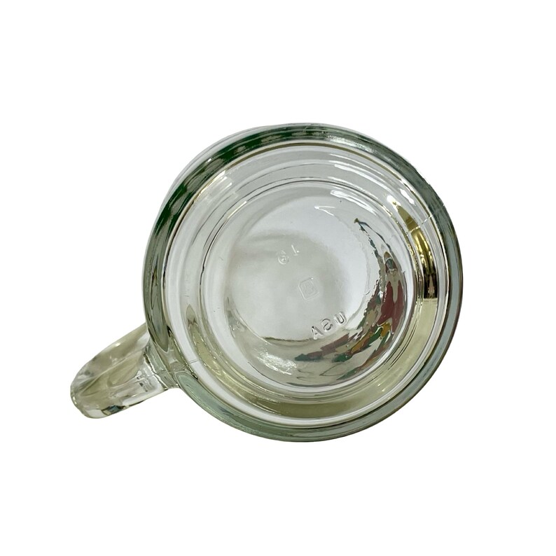 May include: A clear glass mug viewed from the bottom, featuring a circular base with a handle extending to the left. The glass is embossed with the text USA and the number 19, visible through the transparent material of the mug's base.