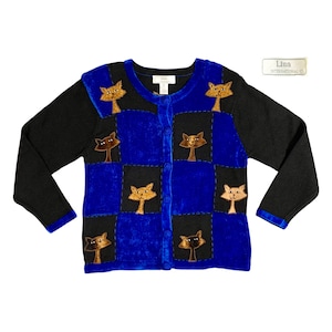 May include: A blue and black cardigan with a patchwork design featuring embroidered cats. The cardigan has a button closure and long sleeves.