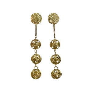 May include: A pair of gold-tone drop earrings featuring a circular filigree stud connected by a short chain to three vertically aligned, spherical filigree beads. The metal components exhibit an intricate, openwork scroll pattern throughout.