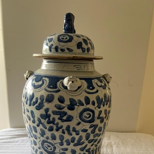 Könnte beinhalten: Eine große, blau-weiße Keramikvase mit Deckel. Die Vase hat ein Blumendesign und kleine, löwenartige Griffe. Der Deckel hat einen Knauf und ein Blumenmuster. Die Vase wird wahrscheinlich zu dekorativen Zwecken verwendet.