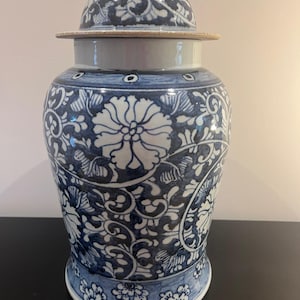 Può includere: Un barattolo per zenzero in ceramica con coperchio, caratterizzato da una base bianca decorata con intricati motivi floreali blu e disegni di viticci. Il vaso ha un corpo arrotondato, un collo stretto e un coperchio a cupola abbinato.
